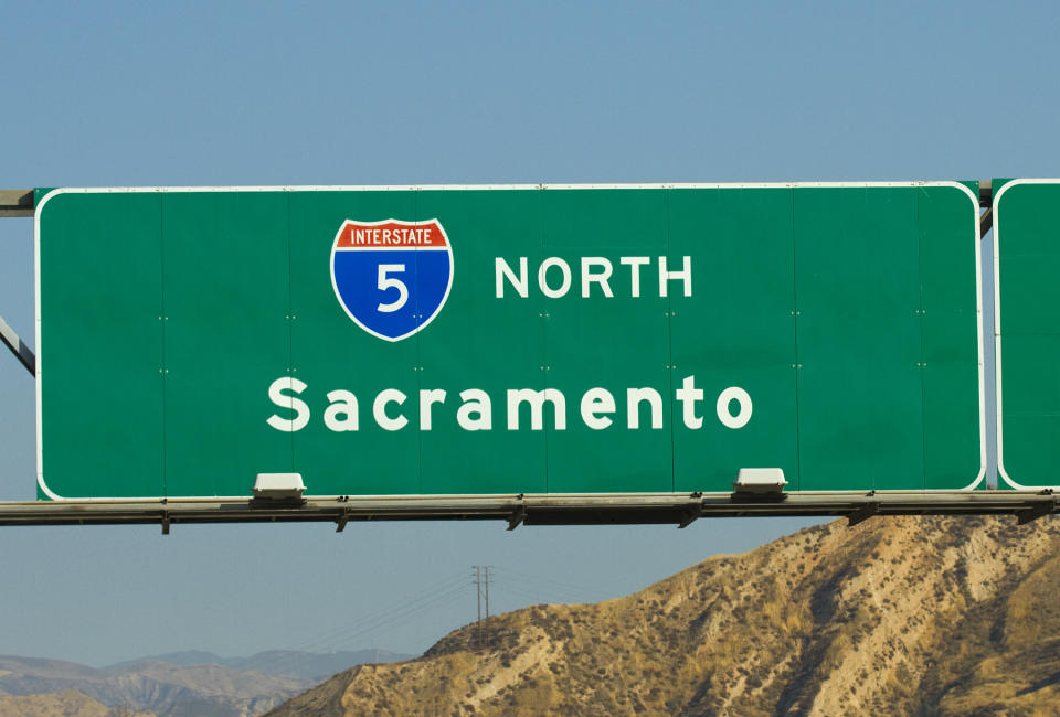 A green highway sign reading "Interstate 5 North Sacramento" with mountains in the background