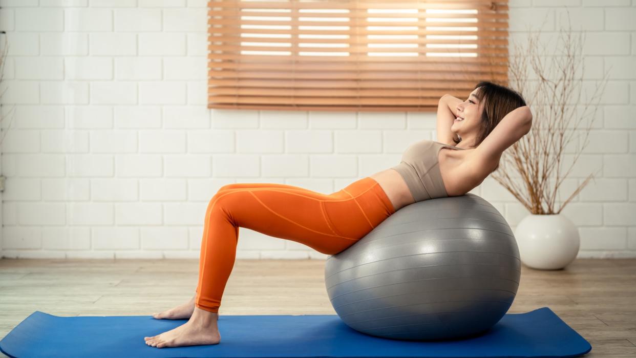  Woman laying on her back on a Stability ball with hands behind head and feet on exercise mat. 