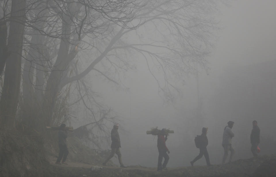 In this Jan. 15, 2020, photo, Nepalese men carry logs of wood for a cremation, enveloped in thick morning fog in Bhaktapur, Nepal. (AP Photo/Niranjan Shrestha, File)