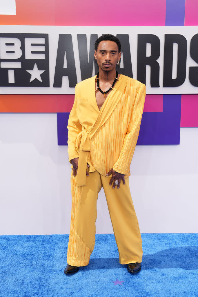 Durand Bernarr  in a fashionable, asymmetrical yellow suit stands on the red carpet at the BET Awards