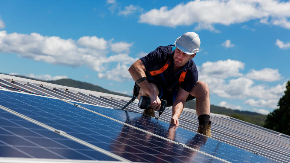 Solar panel installer with drill installing solar panels on roof on a sunny day.