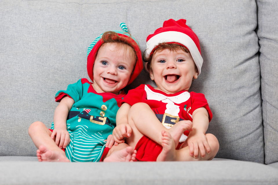 Lucas wearing an elf outfit and Bailey right in a Santa outfit on a couch. 