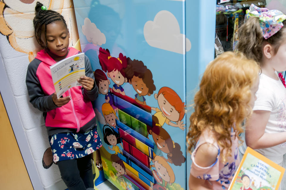 FILE - Janaya Sells, 7, reads a token-bought book on Sept. 26, 2019, during a ribbon cutting for an Inchy the Worm book vending machine at R.E. Stevenson Elementary School in Russellville, Ky. For decades, there has been a clash between two schools of thought on how to best teach children to read, with passionate backers on each side of the so-called reading wars. But the approach gaining momentum lately in American classrooms is the so-called science of reading. (Bac Totrong/Daily News via AP, File)