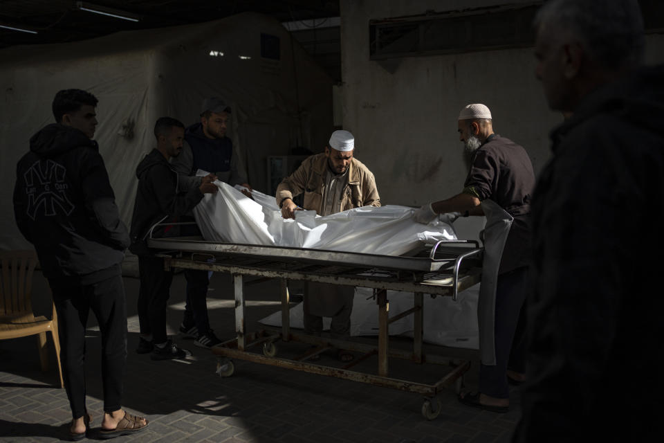 Palestinians carry the body of a person killed in the Israeli bombardment of the Gaza Strip, outside the morgue in Rafah, southern Gaza, Friday, Dec. 22, 2023. (AP Photo/Fatima Shbair)