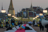 Officials adjust a carpet as late King Bhumibol Adulyadej's images is displayed in the background ahead of the arrival of King Maha Vajiralongkorn and Queen Suthida to participate in a candle lighting ceremony to mark birth anniversary of late King Bhumibol Adulyadej at Sanam Luang ceremonial ground in Bangkok, Thailand, Saturday, Dec. 5, 2020. (AP Photo/Gemunu Amarasinghe)