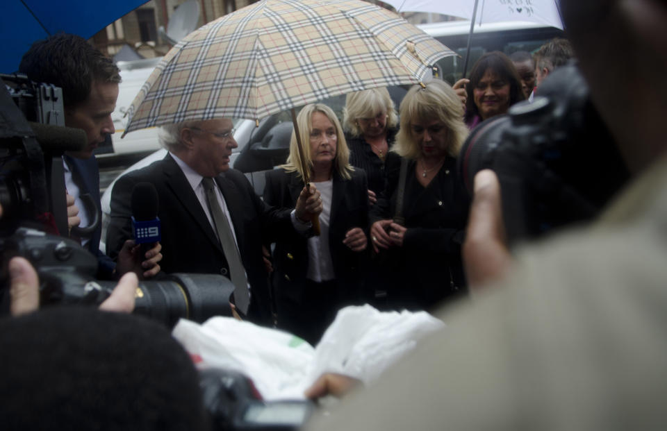 June Steenkamp, center under umbrella, the mother of Reeva Steenkamp, arrives at the High Court in Pretoria, South Africa, Monday, March 3, 2014. Athlete Oscar Pistorius is charged with murder with premeditation in the shooting death of his girlfriend Reeva Steenkamp in the pre-dawn hours of Valentine's Day 2013. (AP Photo/Skyler Reid)