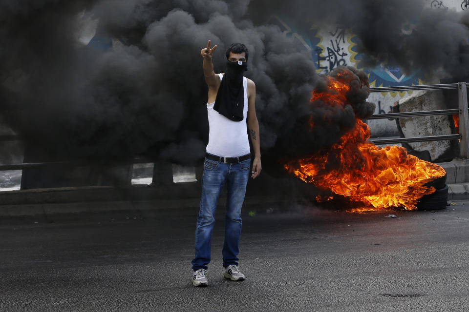 An anti-government protester makes victory sign next to tires that were set on fire to block a road during a demonstration, in Beirut, Lebanon, Sunday, Sept. 29, 2019. Hundreds of Lebanese are protesting an economic crisis that has worsened over the past two weeks, with a drop in the local currency for the first time in more than two decades. (AP Photo/Bilal Hussein)