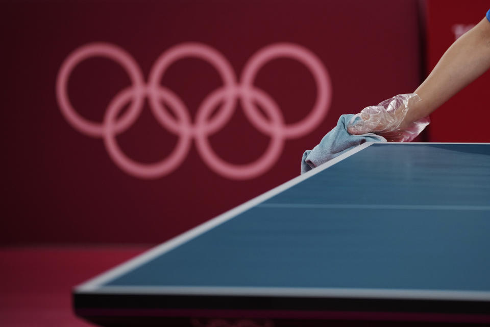 A staff member cleans the table during table tennis mixed doubles round of 16 matches at the 2020 Summer Olympics, Saturday, July 24, 2021, in Tokyo. (AP Photo/Kin Cheung)