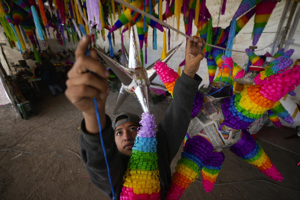 Un trabajador cuelga una piñata con la tradicional forma de esfera con siete picos, que se rellena con frutas y dulces, en un negocio familiar en Acolman, al norte de Ciudad de México, el miércoles 13 de diciembre de 2023. Esta artesanía tradicional tiene un origen religioso y está cargada de simbolismo: cada cono representa uno de los siete pecados capitales, por eso se golpea la piñata hasta destruirla como una forma de alejarse de esos pecados. (AP Foto/Fernando Llano)