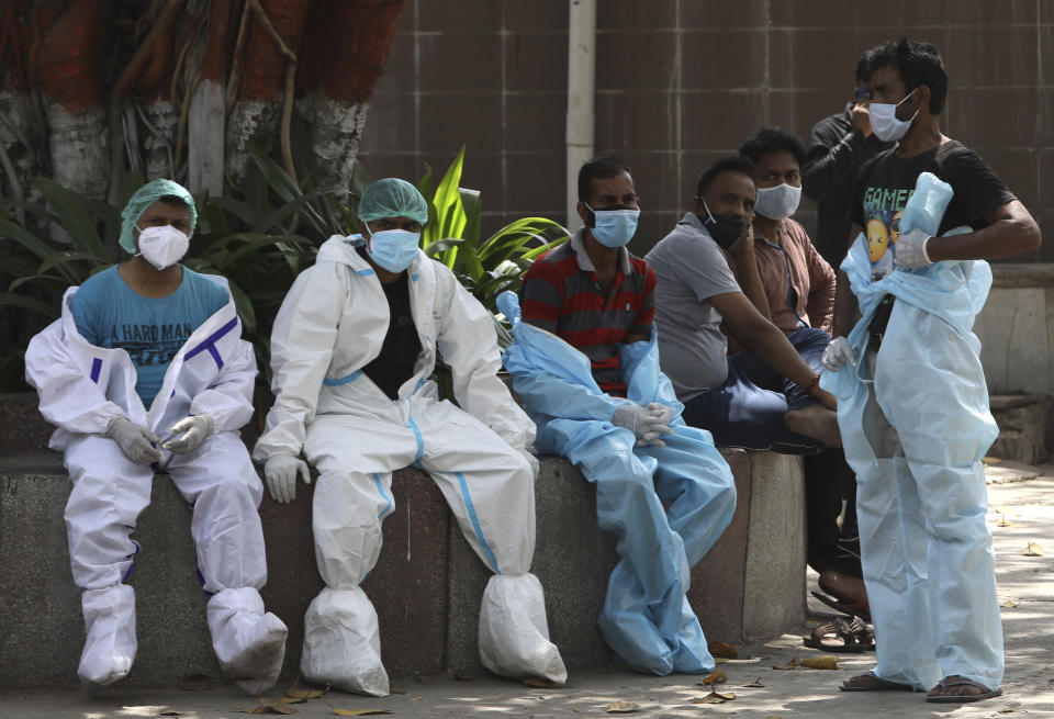 Health workers rest in between cremating COVID-19 victims in New Delhi, India, Monday, April 19, 2021. India has been overwhelmed by hundreds of thousands of new coronavirus cases daily, bringing pain, fear and agony to many lives as lockdowns have been placed in Delhi and other cities around the country. (AP Photo/Manish Swarup)