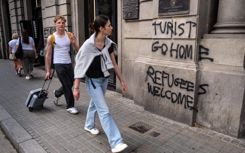 A young couple is seen walking past anti-tourism graffiti in Barcelona