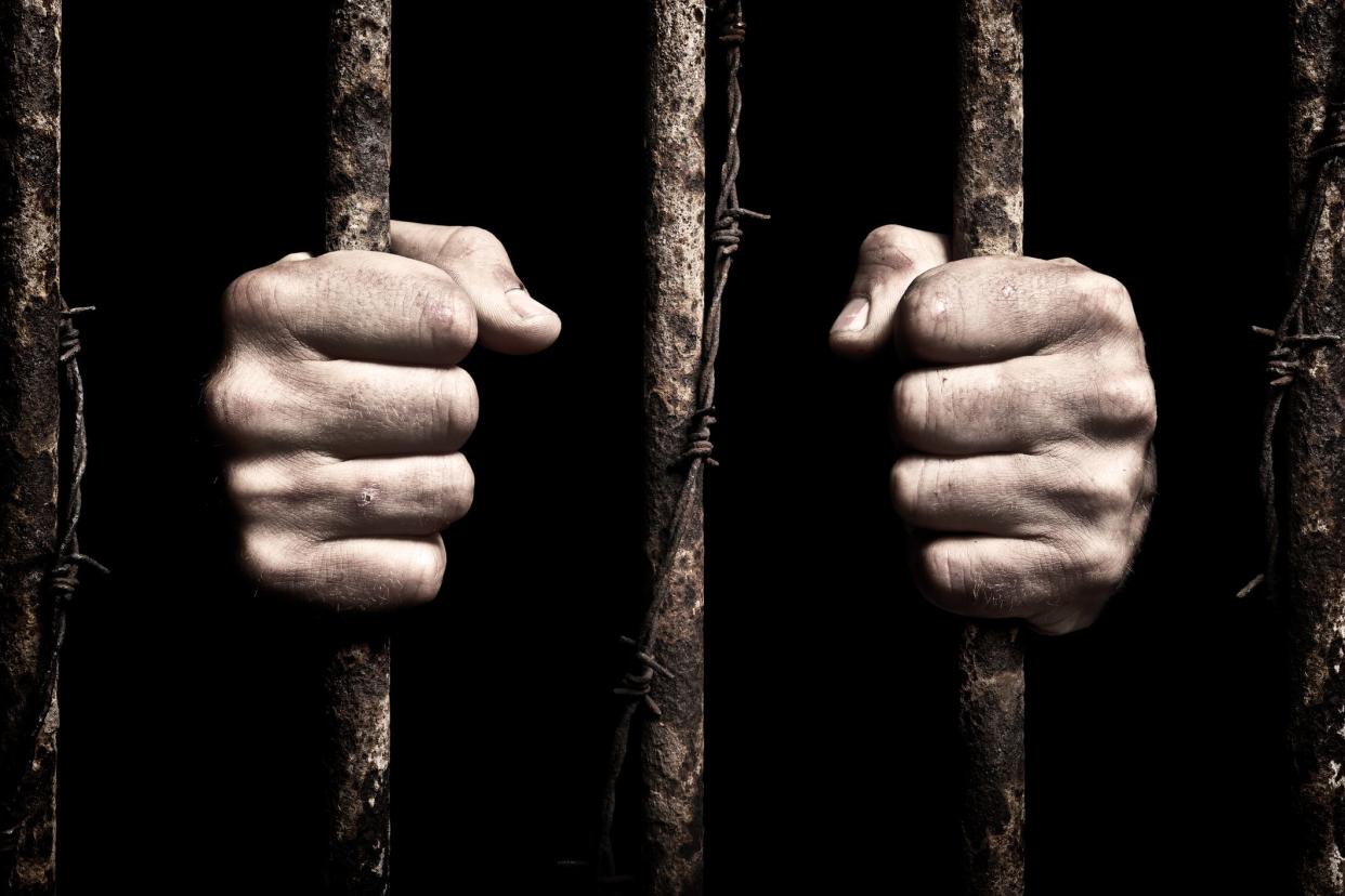 Hands grip prison bars.