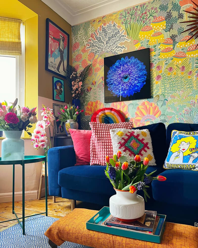 Decorative pillows on blue velvet sofa in colorful wallpapered living room.