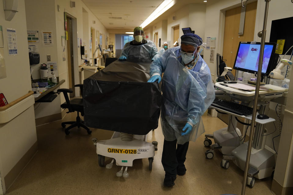 Transporters Miguel Lopez, front, and Noe Meza wheel a gurney carrying a deceased COVID-19 patient at Providence Holy Cross Medical Center in the Mission Hills section of Los Angeles, Saturday, Jan. 9, 2021. (AP Photo/Jae C. Hong)