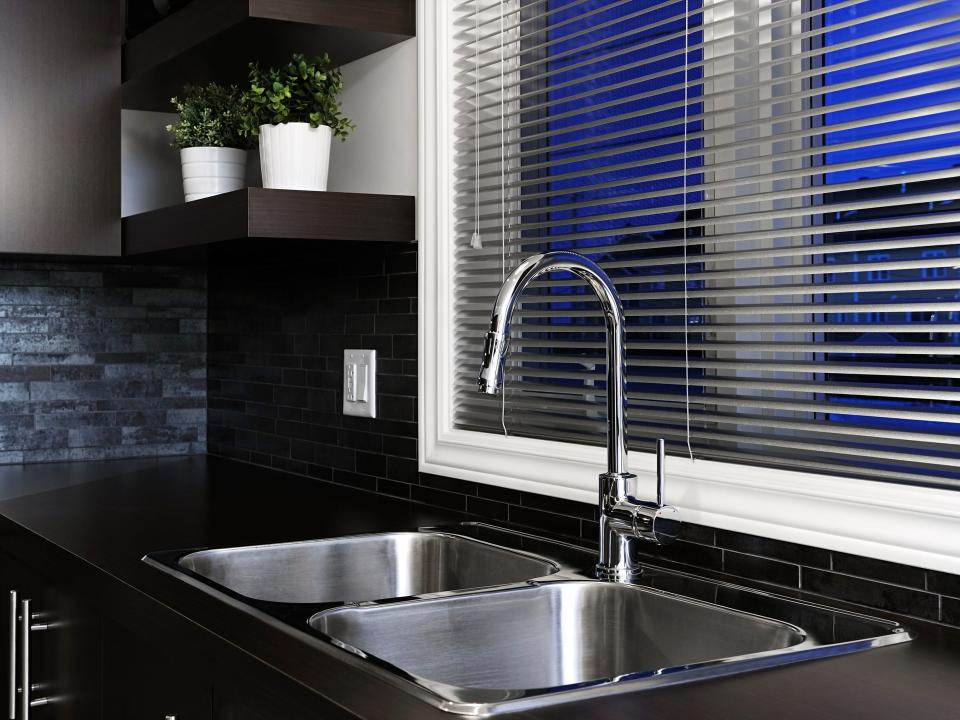 A black kitchen with a silver sink and metal blinds