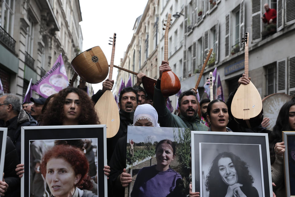 Kurdish activists hold portraits and music instruments at the site where three women Kurdish activists were found shot dead in 2013, Monday, Dec. 26, 2022 in Paris. A 69-year-old Frenchman is facing preliminary charges of racially motivated murder, attempted murder and weapons violations over last Friday's shooting, prosecutors said. The shooting shocked and infuriated the Kurdish community in France. ( AP Photo/Lewis Joly)