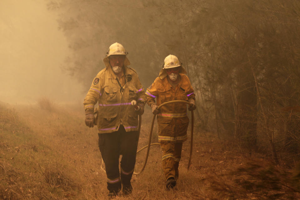 Firefighters drag their water hose after putting out a spot fire near Moruya, Australia, Saturday, Jan. 4, 2020. Australia's Prime Minister Scott Morrison called up about 3,000 reservists as the threat of wildfires escalated Saturday in at least three states with two more deaths, and strong winds and high temperatures were forecast to bring flames to populated areas including the suburbs of Sydney. (AP Photo/Rick Rycroft)