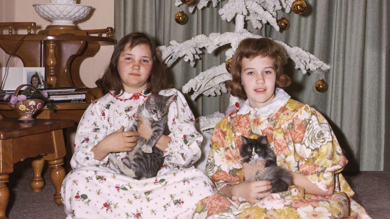 portrait of caucasian sisters wearing pajamas holding cats on christmas