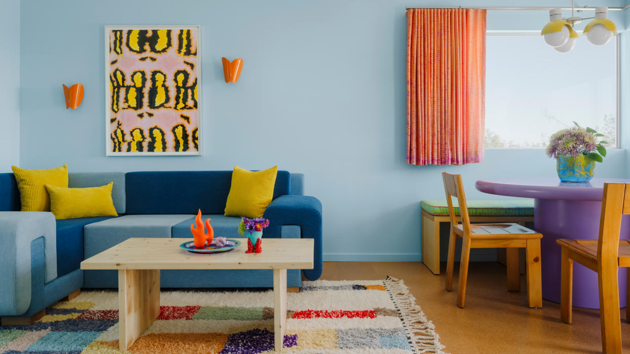  Tonal blue denim sofa against light blue wall with orange sconces and yellow artwork. 