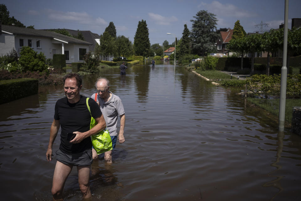 FILE - In the July 17, 2021 file photo, father and son walk through their flooded street, in the town of Brommelen, Netherlands. Dutch climate experts warned Monday, Oct. 25, 2021 that the low-lying Netherlands could face higher sea level rises than previously forecast as well as the threat of extreme rainfall and other dangerous weather events caused by climate change. (AP Photo/Bram Janssen)