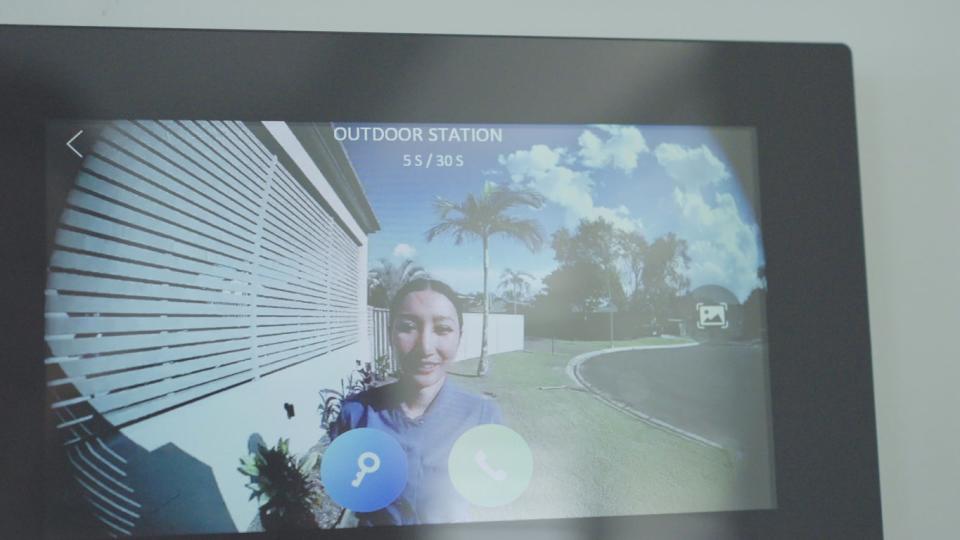 Security camera footage of a person standing at a house's front door. 