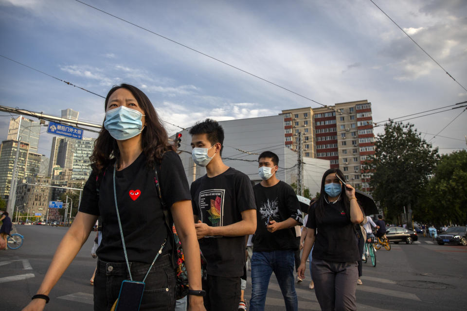 People wearing face masks to help protect against the spread of the coronavirus cross an intersection in Beijing, Tuesday, Aug. 4, 2020. Both mainland China and Hong Kong reported fewer new cases of COVID-19 on Tuesday as strict measures to contain new infections appear to be taking effect. (AP Photo/Mark Schiefelbein)