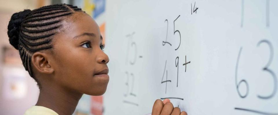 Portrait of Black girl writing solution of sums on white board at school.