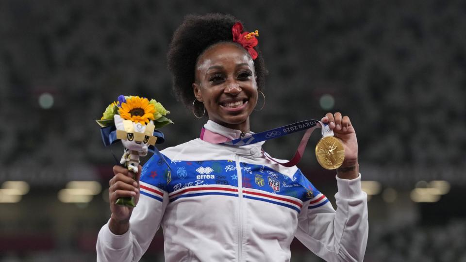 Jasmine Camacho-Quinn holds up flowers and the gold medal around her neck.