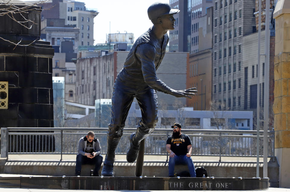 FILE - Baseball fans Chris Miller, right, and Jeff Muster of Pittsburgh, sit near a statue of Pittsburgh Pirates Baseball Hall of Fame outfielder Roberto Clemente, outside PNC Park on what would have been opening day in Pittsburgh, Thursday, April 2, 2020. The 19-foot, 4,000-pound statue of Kobe Bryant in downtown Los Angeles is just the latest example of a sports team honoring a player with this kind of larger-than-life presence. (AP Photo/Gene J. Puskar, File)