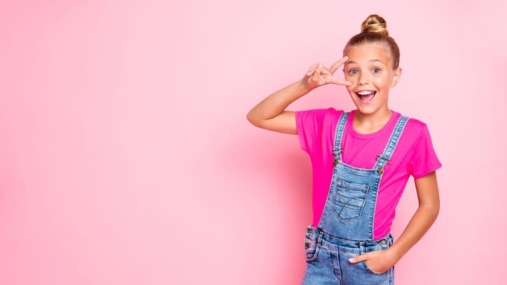 cute cheerful girl showing a peace sign in denim overalls and a pink shirt