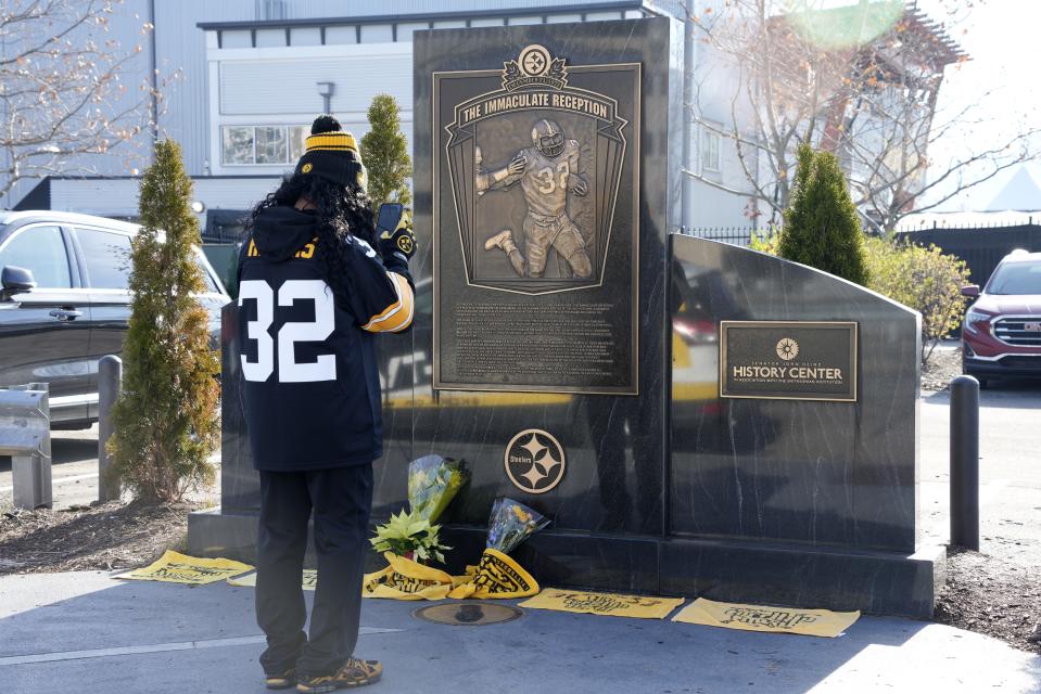 A Steelers fan takes a photo of the flowers and Terrible Towels placed at the Immaculate Reception memorial outside Acrisure Stadium in Pittsburgh.