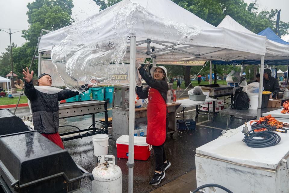 Christine Nguyen knocks water off of a tent during a weather postponement from a heavy rainstorm at Taste of Fort Collins on Sunday.