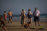 People wearing face masks stay at the beach in Barbate, Cadiz province, south of Spain, on Saturday, July 25, 2020. Ministers are set to remove Spain from the Government's list of safe countries to travel to after the European country saw a rise in Covid-19 cases. The decision means those coming back from Spain will have to self-isolate for two weeks upon their return to England. (AP Photo/Emilio Morenatti)