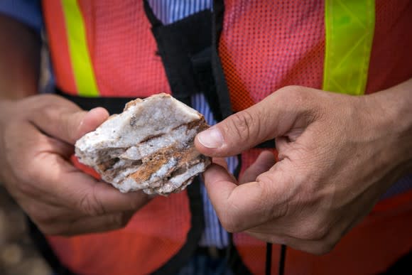Person in safety vest holding a piece of silver ore in hand.
