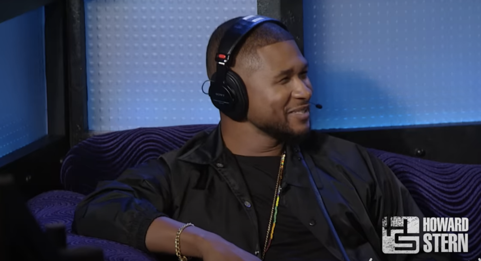 Usher in a studio with headphones smiling, on "The Howard Stern Show"