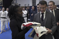 French President Emmanuel Macron, foreground right, receives official French team jerseys as a gift during his visit to France's National Institute of Sport, Expertise, and Performance (INSEP), prior to presenting his New Year's wishes to elite athletes ahead of the Paris 2024 Olympic and Paralympic Games, in Paris, Tuesday, Jan. 23, 2024. (Stephane De Sakutin/Pool Photo via AP)