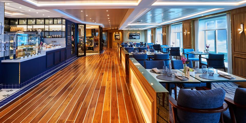 A wood-panelled dining area inside The World with tables and a counter topped with cakes and bakery items.