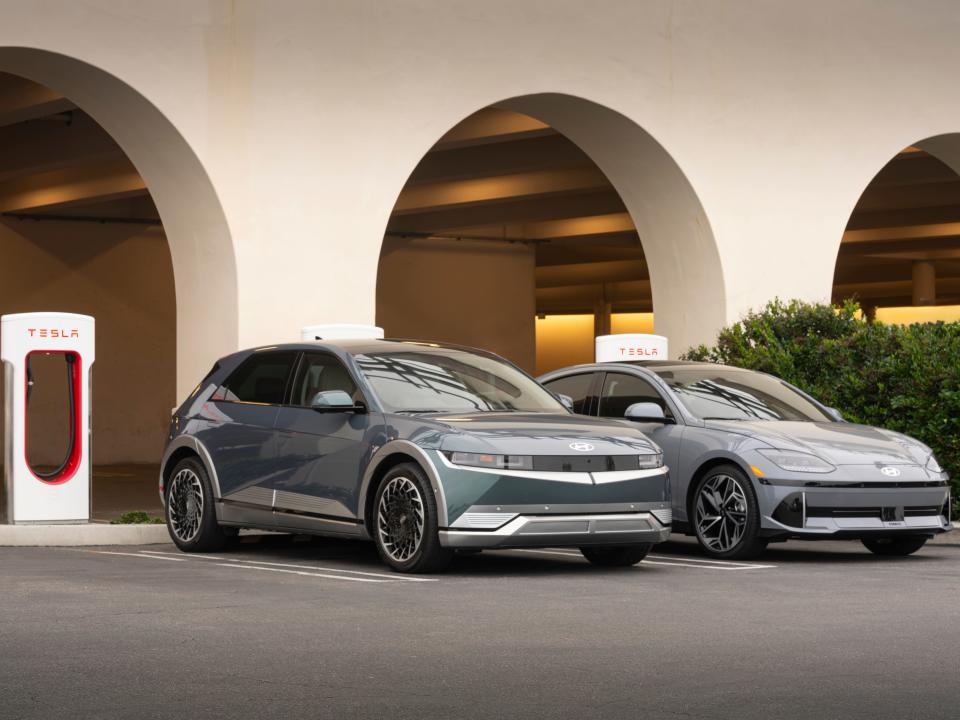 Two Hyundai electric vehicles parked in front of Tesla chargers.