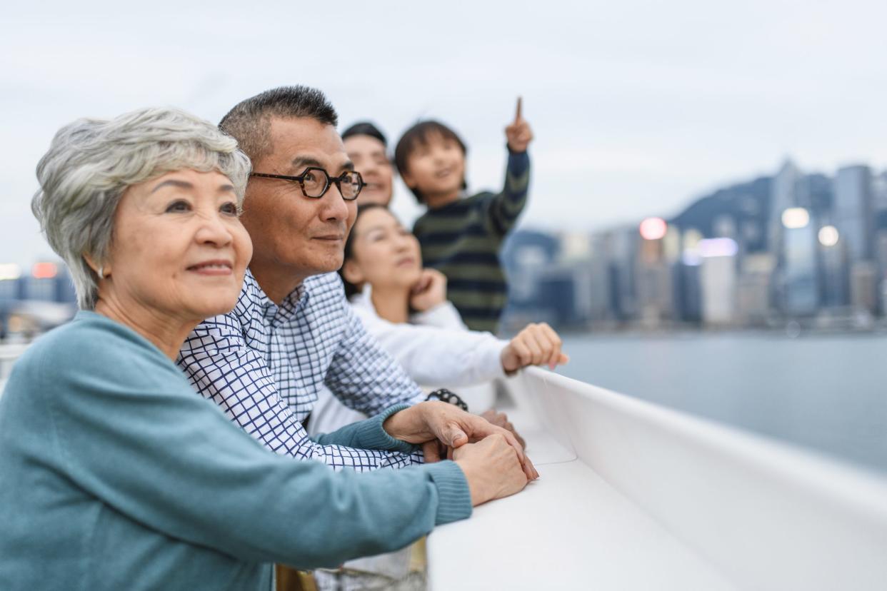 Relaxed senior Chinese woman and husband enjoying Hong Kong views with extended family at Ocean Terminal Deck atop Harbour City Shopping Centre.