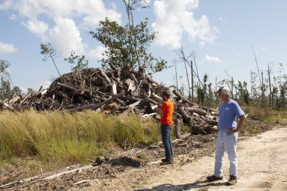 In this Oct. 5, 2019 photo, Daniel Leonard and his father Joe, right, stand near a heap of lumber on their family's property. The massive storm killed more than two dozen people in northern Florida, destroyed hundreds of homes and brought catastrophic damage to the region’s timber industry. (AP Photo/Bobby Caina Calvan)