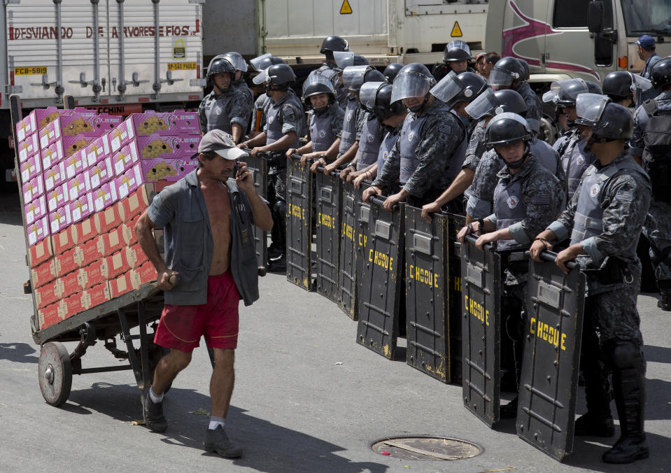 A man pulls a cart of boxed fruit past a cordon of riot police standing guard at the CEAGESP complex, the largest food market in Latin America, in Sao Paulo, Brazil, March 14, 2014. Earlier truck drivers protesting a hike in parking fares at the complex, set vehicles on fire and damaged parking ticket booths. (AP Photo/Andre Penner)