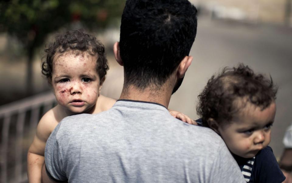 A Palestinian man leaving a hospital holds his daughters after they were injured by an Israeli tank attack during the 2014 Gaza war - MAHMUD HAMS /AFP