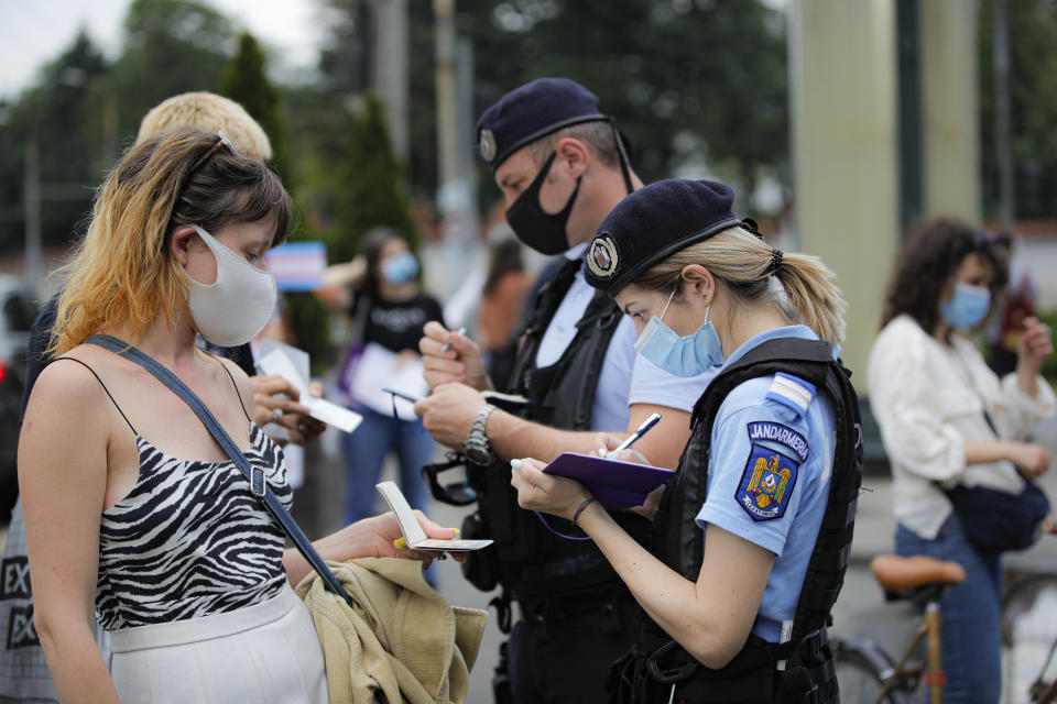 Protesters hold identity papers as gendarmes check participants outside the presidential palace in Bucharest, Romania, Thursday, June 18, 2020, during a rally against a law banning the teaching of gender studies. Dozens of protesters gathered outside Bucharest's Cotroceni Presidential Palace, to express their opposition to a law banning the teaching of gender studies in the country's schools and universities and call on President Klaus Iohannis to reject signing the bill and send it back to parliament. (AP Photo/Vadim Ghirda)