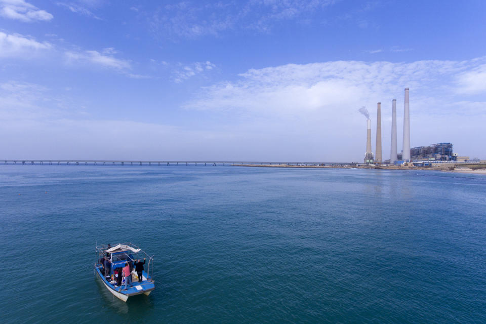 This Monday, Jan. 21, 2019 photo taken by a drone camera, shows researchers from the predator project at the Morris Kahn Marine Research Station established by the University of Haifa look for sharks in Mediterranean Sea off the coast of the northern Israeli city of Hadera. A giant power plant with billowing smoke may not look like the most natural habitat for sea life, but the hot water gushing from an industrial plant in Israel's northern city of Hadera draws schools of sharks that are increasingly endangered by overfishing. (AP Photo/Ariel Schalit)