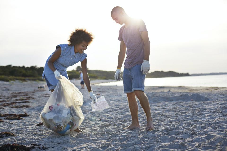 A man and woman pick up plastic waste on a beach.