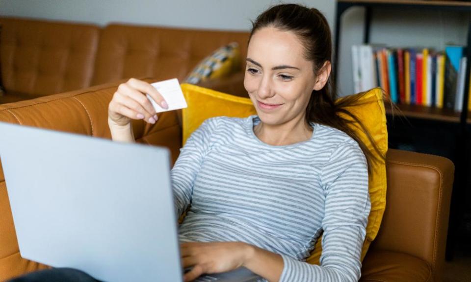 A smiling young woman with a laptop on her knee and a card in her hand