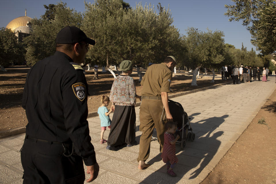 An Israeli police officer escorts a Jewish couple strolling the grounds of the Temple Mount, known to Muslims as the Noble Sanctuary, on the Al-Aqsa Mosque compound in the Old City of Jerusalem, Tuesday, Aug. 3, 2021. Once unthinkable, Jewish morning prayers at Jerusalem's contested holy site, have become the new norm in recent years, flying in the face of longstanding convention. (AP Photo/Maya Alleruzzo)