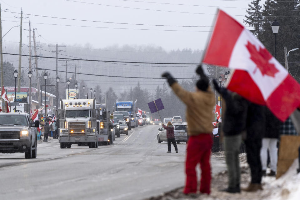 Protesters and supporters against a COVID-19 vaccine mandate for cross-border truckers cheer as a parade of trucks and vehicles pass through Kakabeka Falls outside of Thunder Bay, Ontario, on Wednesday, Jan. 26, 2022. (David Jackson/The Canadian Press via AP)