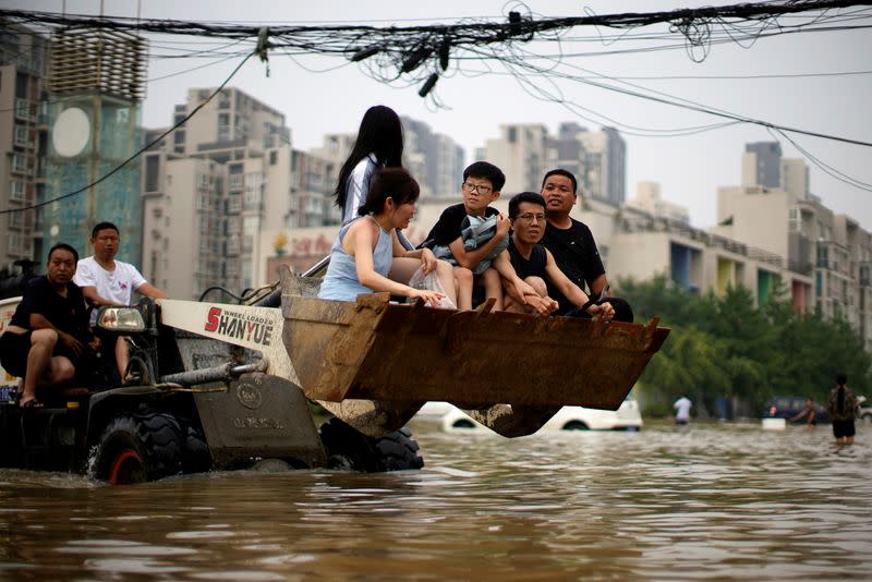 FILE PHOTO: People ride on a front loader as they make their way through floodwaters following heavy rainfall in Zhengzhou