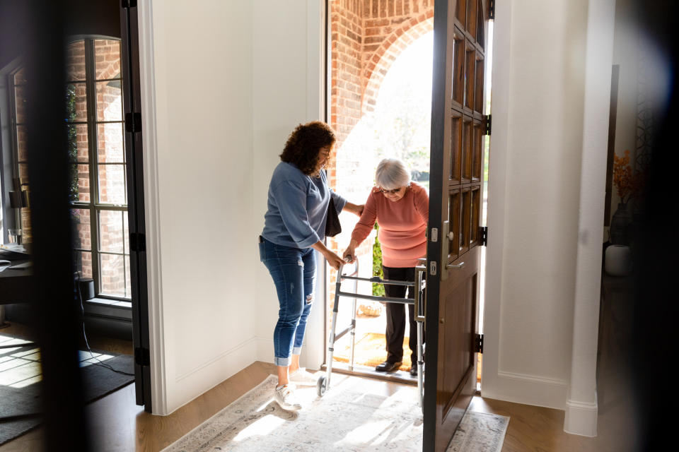 A woman is helping their elderly mom into the house